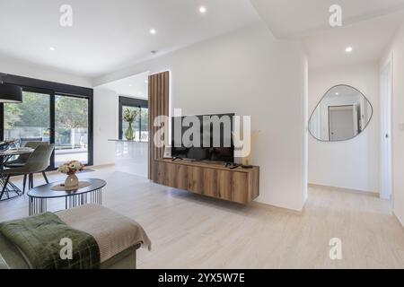 Ein helles und luftiges Wohnzimmer mit elegantem Holzfernseher, Essbereich, großen Glastüren und minimalistischer Einrichtung. Stockfoto