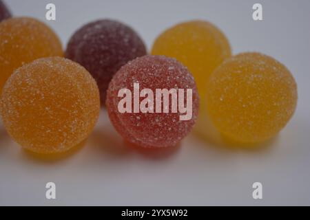 Originale finnische Gelee-Bonbons in Form von runden Kugeln, die mit weißem Zucker bedeckt sind. Gelbe, orange, kirschrote, gummirote Bonbons sind auf einem weißen Plastik. Stockfoto