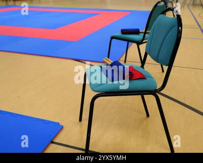 Ein Stuhl mit blau-roten Fahnen vor einem Tatami in einer Sporthalle, symbolisiert die Vorbereitung auf ein aufregendes Kampfsportfest. Stockfoto