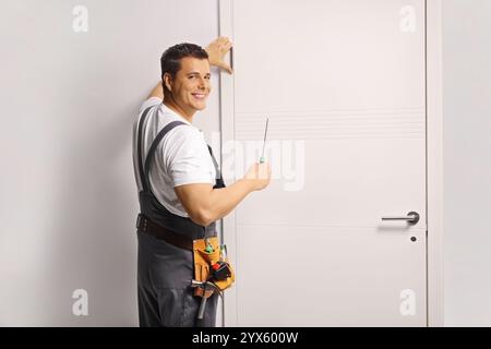 Arbeiter in Uniform, die eine Zimmertür installiert und lächelt Stockfoto