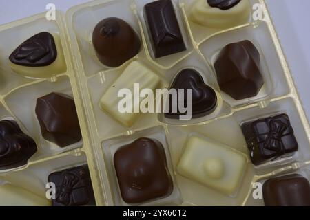 Wunderschöne belgische Schokolade aus weißer, Milch- und Zartbitterschokolade. Große leckere Süßigkeiten mit verschiedenen Füllungen sind in goldenem Kunststoff angeordnet. Stockfoto