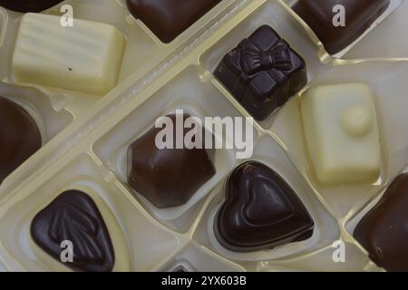 Wunderschöne belgische Schokolade aus weißer, Milch- und Zartbitterschokolade. Große leckere Süßigkeiten mit verschiedenen Füllungen sind in goldenem Kunststoff angeordnet. Stockfoto