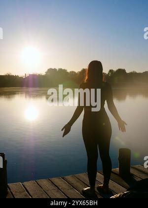 Frau, die auf Sadhu-Brett steht, Prozess des barfuß auf Nägeln, Yoga-Praxis und Meditation im Freien, Herbsttag in der Nähe des Sees bei Sonnenaufgang Stockfoto