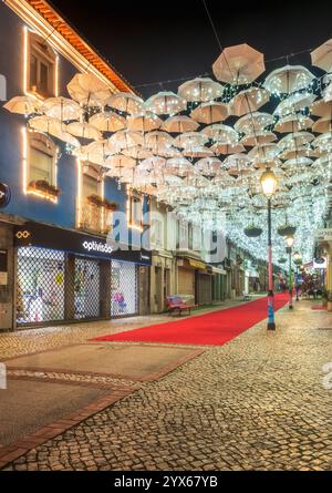 Águeda, Portugal - 27. November 2024: Nächtlicher Blick auf die Straße im Stadtzentrum von Águeda in Portugal, bedeckt mit weißen Regenschirmen mit weihnachtsbeleuchtung. Stockfoto