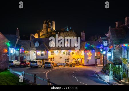 Corfe Castle, Dorset, Großbritannien. Dezember 2024. Die beleuchteten Ruinen von Corfe Castle in Dorset ragen über dem Greyhound Pub im Zentrum des Dorfes hervor, der für die Weihnachtsfeiertage mit bunten Lichtern beleuchtet wurde. Die Burgruine ist heute (13. Dezember) und morgen (14. Dezember) für Besucher geöffnet, damit sie die festlichen Lichter des Winters erleben können. Das Schloss wurde ab 16:00 Uhr mit warmen Lichtern und Feuerstellen beleuchtet, was einen wunderschönen Glanz über die Ruinen erzeugt, den Besucher erkunden können. Es gibt Feuerstellen, in denen Besucher sich sammeln und auf Sumpfmoor stoßen können Stockfoto