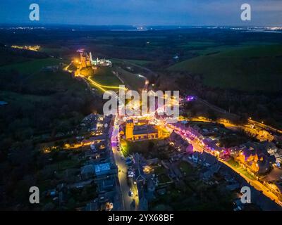 Corfe Castle, Dorset, Großbritannien. Dezember 2024. Die Häuser, Geschäfte und Pubs rund um den malerischen Dorfplatz und die Kirche von Corfe Castle in Dorset wurden mit bunten Lichtern für die Weihnachtsfeiertage dekoriert. Bildnachweis: Graham Hunt/Alamy Live News Stockfoto