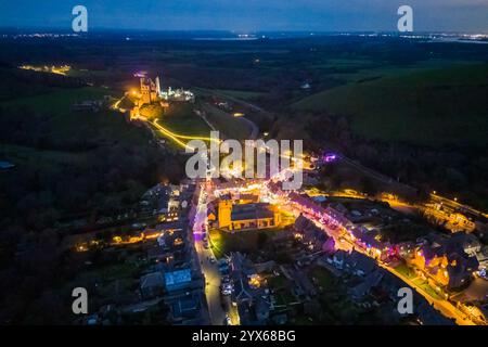 Corfe Castle, Dorset, Großbritannien. Dezember 2024. Die Häuser, Geschäfte und Pubs rund um den malerischen Dorfplatz und die Kirche von Corfe Castle in Dorset wurden mit bunten Lichtern für die Weihnachtsfeiertage dekoriert. Bildnachweis: Graham Hunt/Alamy Live News Stockfoto