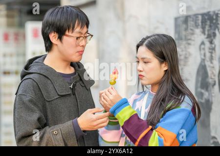 Junge chinesische Paare in ihren 20ern essen Pekings berühmte Zuckerbonbons auf einem Bürgersteig im Bezirk Hongkou, Shanghai, Volksrepublik Stockfoto
