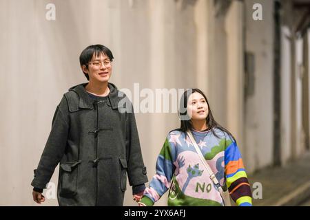 Ein junges chinesisches Paar im Alter von 20 Jahren, das in der kalten Jahreszeit auf dem Gehweg im Bund, Hongkou District, Shanghai, Volksrepublik China läuft Stockfoto