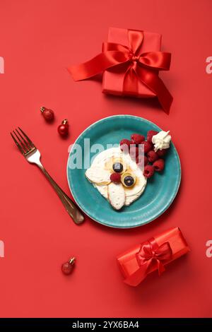 Teller mit Pfannkuchen in Form des Weihnachtsmanns auf rotem Hintergrund. Weihnachtsfeier Stockfoto