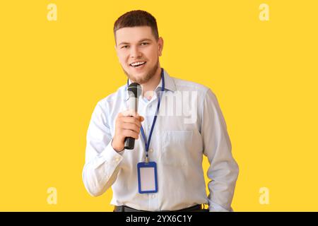 Männlicher Reporter mit Mikrofon und leerem Namensschild auf gelbem Hintergrund Stockfoto