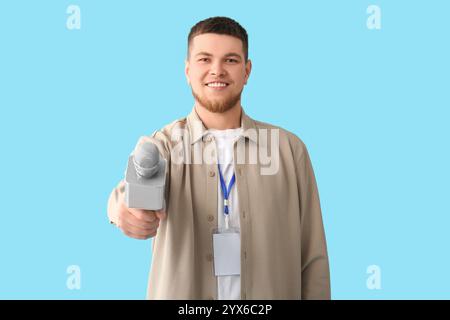 Männlicher Reporter mit Mikrofon und leerem Namensschild, der ein Interview auf blauem Hintergrund macht Stockfoto