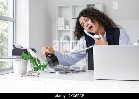 Junge afroamerikanische Geschäftsfrau mit Wecker, die telefonisch spricht und versucht, die Frist im Amt einzuhalten Stockfoto