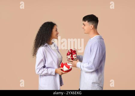 Liebevolles junges Paar, das Geschenkboxen auf beigefarbenem Hintergrund austauscht. Valentinstag-Feier Stockfoto