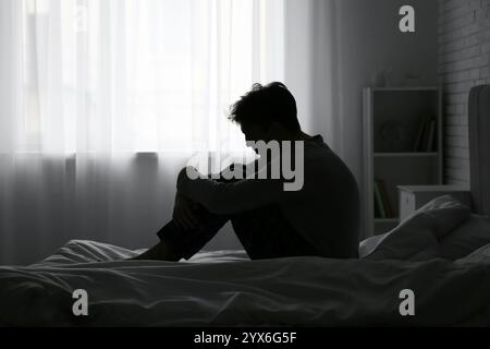 Silhouette eines depressiven jungen Mannes, der in einem dunklen Schlafzimmer sitzt Stockfoto