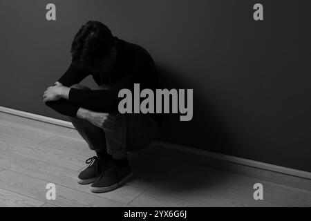 Depressiver junger Mann, der in der Nähe einer dunklen Wand sitzt Stockfoto