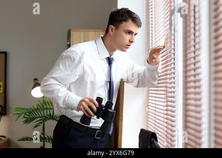 Männlicher FBI-Agent mit Fernglas, der im Büro im Fenster schaut Stockfoto