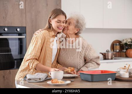 Eine ältere Frau küsst ihre Enkelin mit leckerem Kuchen in der Küche Stockfoto