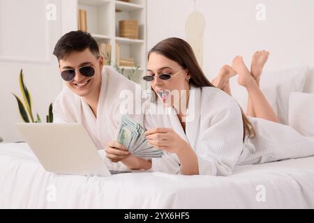 Cooles junges Paar mit Geld und Laptop im Schlafzimmer Stockfoto