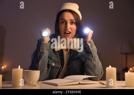 Schockierte die junge Frau mit Taschenlampen und Buch zu Hause, während der Blackout ausfiel Stockfoto