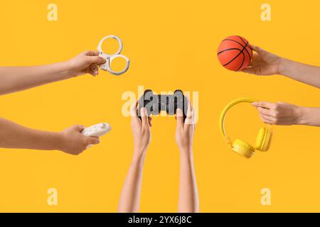 Weibliche Hände mit Spielpad, Kopfhörern, Handschellen und Ball auf gelbem Hintergrund Stockfoto