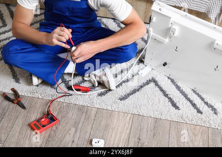 Männlicher Techniker, der die Spannung von elektrischen Konvektorheizungen im Schlafzimmer misst Stockfoto