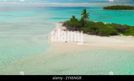 Frau, die am weißen Strand mit türkisfarbenem Wasser, Palmen, üppigem Grün und klarem blauen Himmel spaziert, schafft ein ruhiges tropisches Paradies Stockfoto