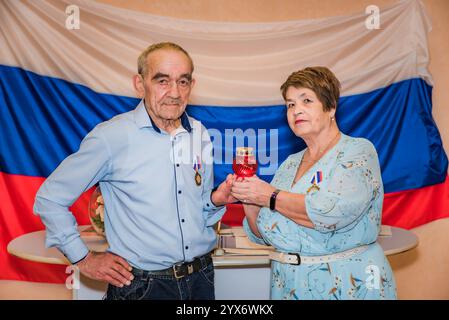 Älteres russisches Ehepaar feiert ihren goldenen Hochzeitstag in einem Standesamt, steht vor russischer Flagge und hält ein Orthodo Stockfoto