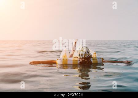 Frau, Schwimmer, Ozean - Frau, die einen gelben Badeanzug trägt, schwimmt auf einem gelb-weiß gestreiften Schwimmbecken mitten im Ozean. Stockfoto