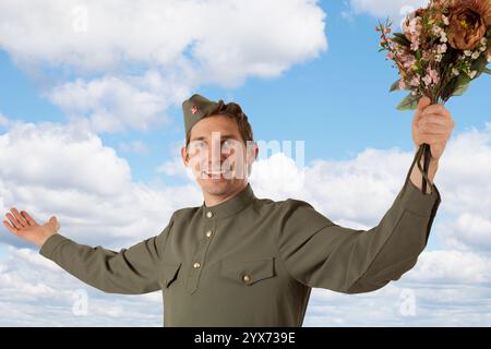 Sowjetischer Soldat in Uniform des Zweiten Weltkriegs mit einem Blumenstrauß auf dem Hintergrund des blauen Himmels Stockfoto