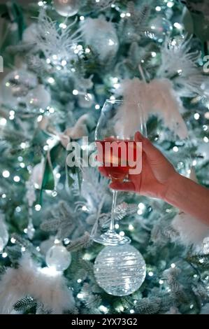 Die Hand der Frauen hält Trinkglas vor dem Weihnachtsbaum Stockfoto