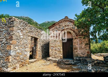 Kleine byzantinische Kirche Agia Kyriaki in Sotirianika, Messinien, Griechenland, umgeben von Steinruinen und üppiger Berglandschaft. Stockfoto