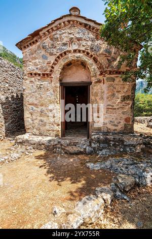 Kleine byzantinische Kirche Agia Kyriaki in Sotirianika, Messinien, Griechenland, umgeben von Steinruinen und üppiger Berglandschaft. Stockfoto