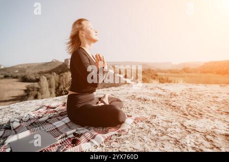 Frau übt Yoga auf einem Berggipfel mit Laptop Stockfoto