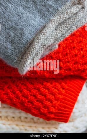 Graue, weiße und leuchtend orange Strickpullover auf einem Stapel. Ein Stapel kuscheliger, handgefertigter Kleidung. Konzept für unterschiedliche Strickmuster. Farbenfrohe gewebte Pullover Stockfoto