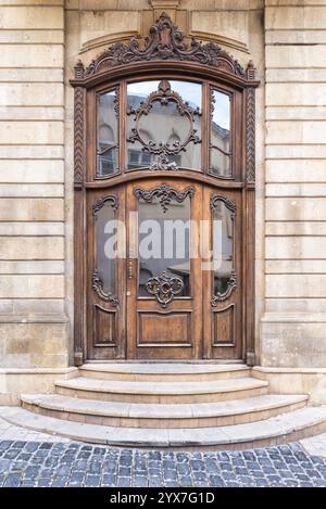 Die wunderschön gefertigte Holztür verfügt über kunstvolle Schnitzereien und eine große Glasscheibe. Es befindet sich in einem historischen Gebäude in Icherisheher, Baku, Aserbaidschan, mit Steinmauern, umgeben von Kopfsteinpflaster Stockfoto