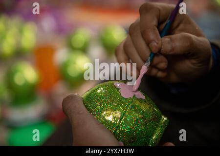 Ein muslimischer Kunsthandwerker aus Kaschmir malt in der Werkstatt vor der Weihnachtsfeier eine Weihnachtskugel aus Pappe-mâché. Mit dem Vorweihnachtsanbruch sind die Handwerker aus Kashmiri Papier-mâché damit beschäftigt, verschiedene festliche Produkte und Ziergegenstände für den Export in die Vereinigten Staaten, Großbritannien, Frankreich, Deutschland und viele andere Teile der Welt zu veredeln. Künstler und Hersteller sagen jedoch, dass der russisch-ukrainische Krieg ihr Geschäft um 60 % reduziert hat und dass sie angesichts des anhaltenden Konflikts darum kämpfen, Aufträge zu erhalten. Diese geopolitischen Schwierigkeiten haben Kreation Stockfoto