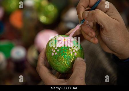 Ein muslimischer Kunsthandwerker aus Kaschmir malt in der Werkstatt vor der Weihnachtsfeier eine Weihnachtskugel aus Pappe-mâché. Mit dem Vorweihnachtsanbruch sind die Handwerker aus Kashmiri Papier-mâché damit beschäftigt, verschiedene festliche Produkte und Ziergegenstände für den Export in die Vereinigten Staaten, Großbritannien, Frankreich, Deutschland und viele andere Teile der Welt zu veredeln. Künstler und Hersteller sagen jedoch, dass der russisch-ukrainische Krieg ihr Geschäft um 60 % reduziert hat und dass sie angesichts des anhaltenden Konflikts darum kämpfen, Aufträge zu erhalten. Diese geopolitischen Schwierigkeiten haben Kreation Stockfoto