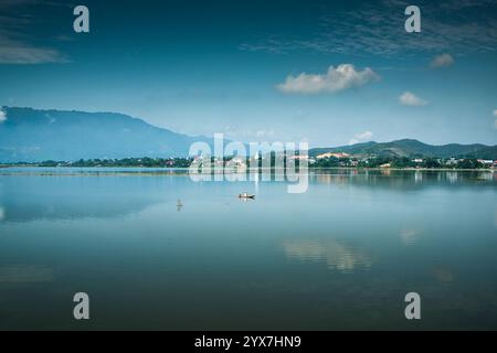 Cleary Lake mit Berg- und Dorfbewohner rudern traditionelles Boot, das sich mit blauem Himmel in der Landschaft von Vietnam spiegelt Stockfoto