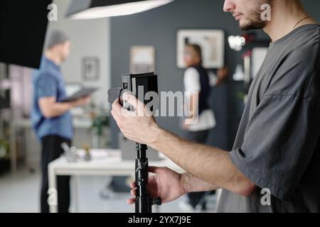 Mittlere Nahaufnahme eines nicht erkennbaren Mannes, der die Kamera auf einem Stativ im Studio justiert Stockfoto