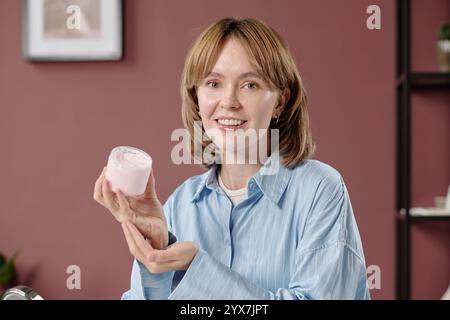 Mittelgroßes Nahporträt einer blonden Frau, die Körperbutter hält, während sie kosmetische Produkte anpreist Stockfoto