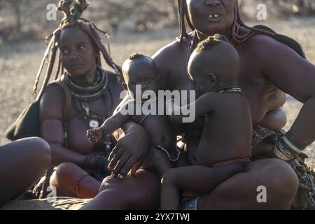 Sie heiratete Himba-Frau mit ihren Babys in den Armen, die vor der Hütte der ersten Frau saßen, morgens im traditionellen Himba-Dorf Kaokove Stockfoto