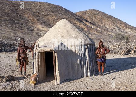 Die verheiratete Himba-Frau lehnt sich an ein traditionelles Lehmhaus, traditionelles Himba-Dorf, Kaokoveld, Kunene, Namibia, Afrika Stockfoto