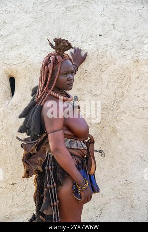 Verheiratet Himba-Frau, die sich an eine traditionelle Lehmhütte lehnt, am Morgen, traditionelles Himba-Dorf, Kaokoveld, Kunene, Namibia, Afrika Stockfoto