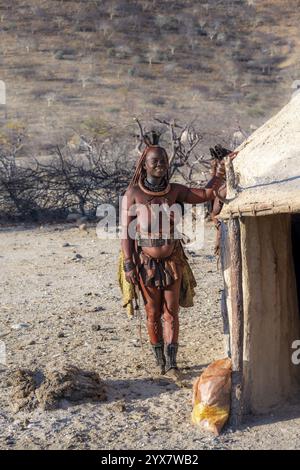 Die verheiratete Himba-Frau lehnt sich an ein traditionelles Lehmhaus, traditionelles Himba-Dorf, Kaokoveld, Kunene, Namibia, Afrika Stockfoto