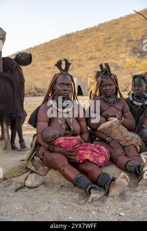 Sie heiratete Himba-Frau mit ihren Babys in den Armen, die vor der Hütte der ersten Frau saßen, morgens im traditionellen Himba-Dorf Kaokove Stockfoto