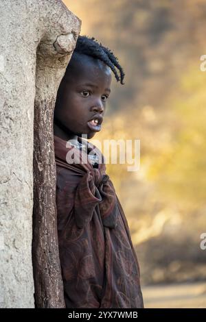 Himba Mädchen lehnt sich an eine traditionelle Lehmhütte, am Morgen, traditionelles Himba Dorf, Kaokoveld, Kunene, Namibia, Afrika Stockfoto