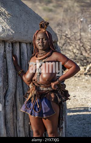 Die verheiratete Himba-Frau lehnt sich an ein traditionelles Lehmhaus, traditionelles Himba-Dorf, Kaokoveld, Kunene, Namibia, Afrika Stockfoto