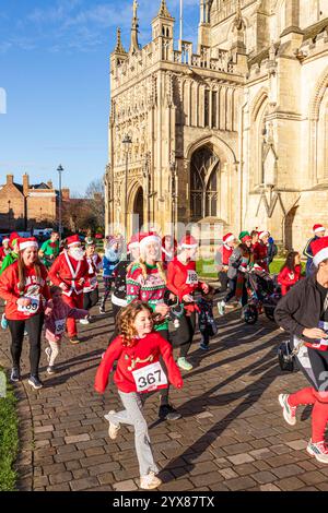 Einige der mehr als 600 Santas passieren die Kathedrale, während sie den Santa Fun Run laufen, der von Rotary International am 14./12/2024 in Gloucester, England U, organisiert wurde Stockfoto