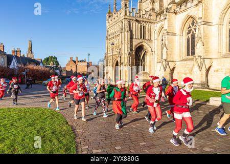 Einige der mehr als 600 Santas passieren die Kathedrale, während sie den Santa Fun Run laufen, der von Rotary International am 14./12/2024 in Gloucester, England U, organisiert wurde Stockfoto